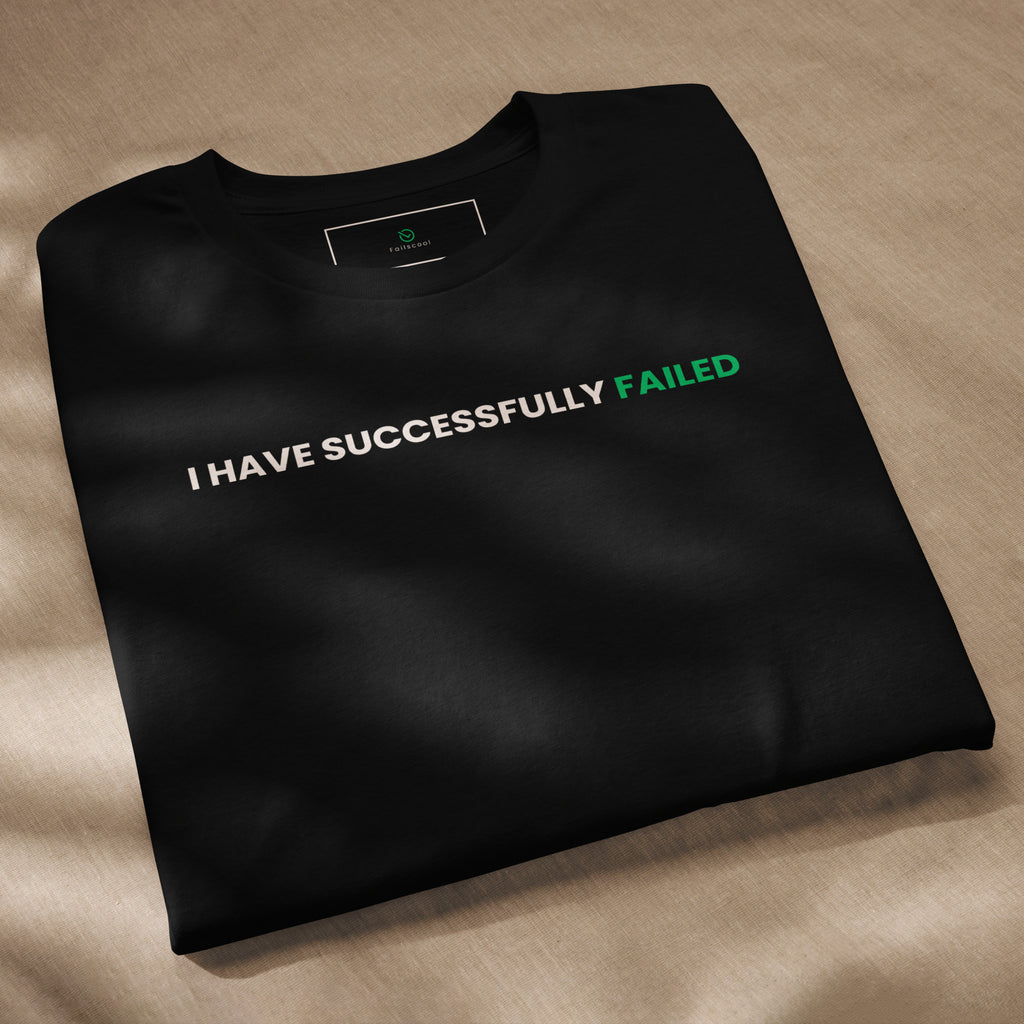 Folded black Failscool t-shirt with the quote “I HAVE SUCCESSFULLY FAILED” clearly visible. Modern, minimalist style.
